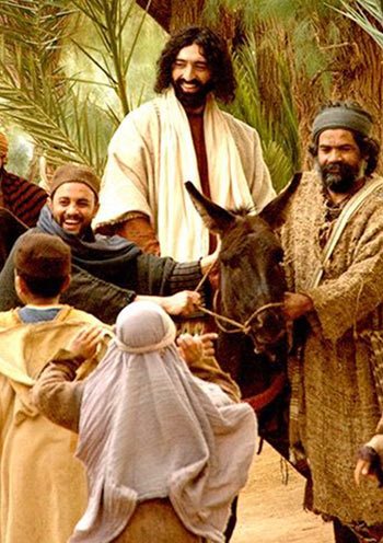Jesus riding a donkey through a happy crowd of people