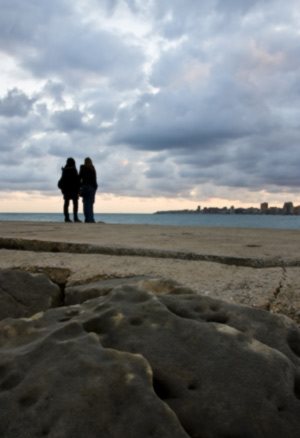 two people standing on a rocky beach looking at a city