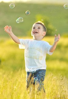 Boy chasing bubbles in a green field