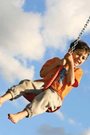 A six-year-old boy swinging against a blue sky with white clouds.