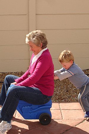 A small boy pushing his grandmother on a plastic play toy.