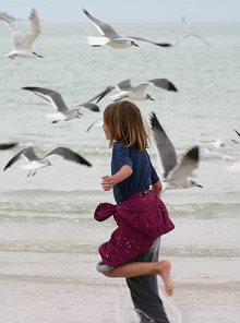 girl running on the beach and seagulls flying around