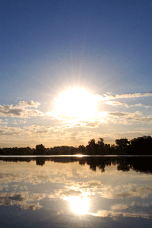 A photograph of the sun rising over a lake.