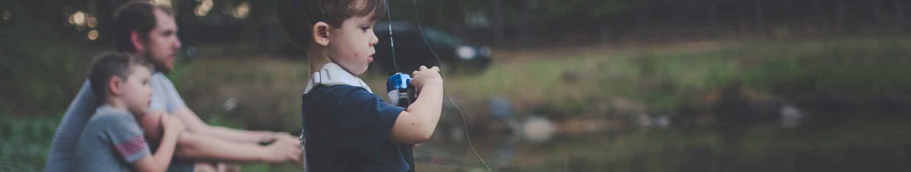 A father and two young sons fishing at a pond at dusk.