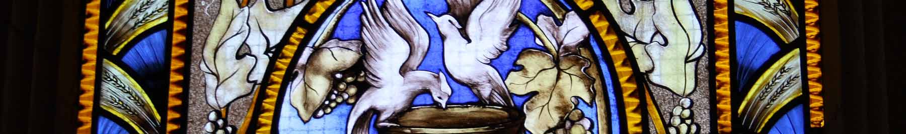 Stained glass window in blue and tan with doves drinking from a fountain in the center.