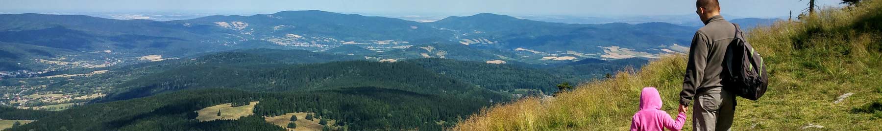 A father and daughter holding hands and looking down into a wide valley below.