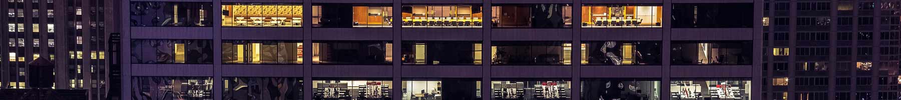Photograph of windows in an office tower taken outside the building at night.