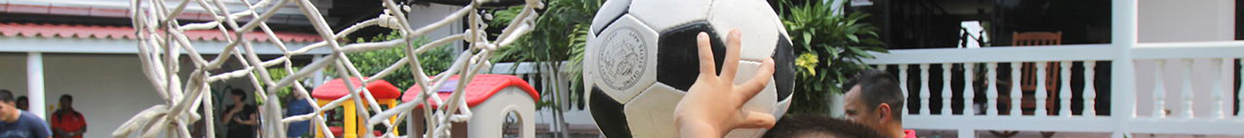 A child playing basketball with a soccer ball; in this slice of the image, only his hands and the ball are visible.