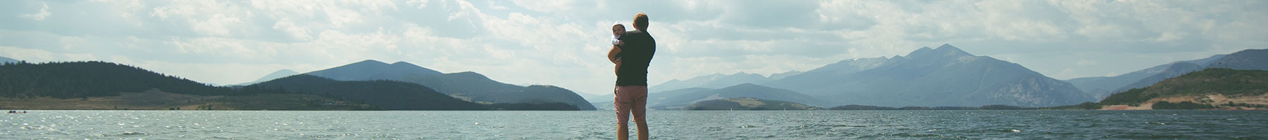 Father holding child and looking across lake with mountains behind
