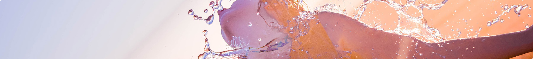 A woman finishing a race, with water splashing over and sun shining behind her.