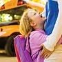 A girl hugging her mother in front of a school bus.