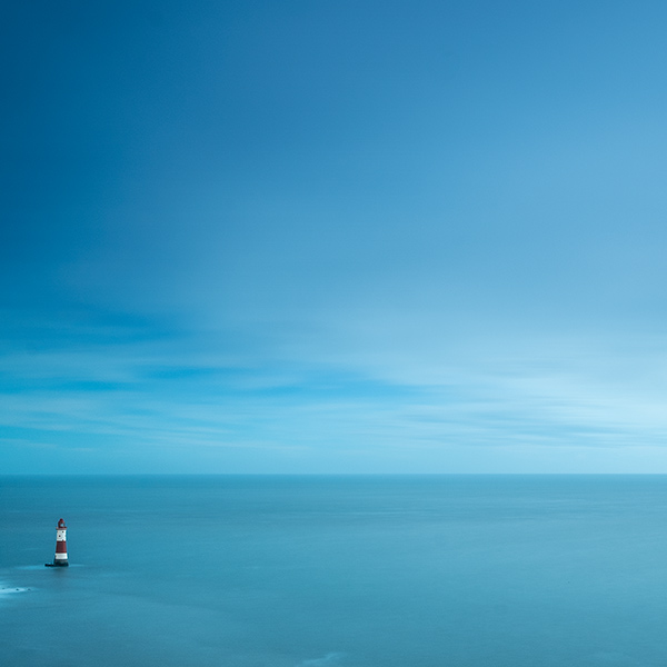 tiny lighthouse by huge sea and sky