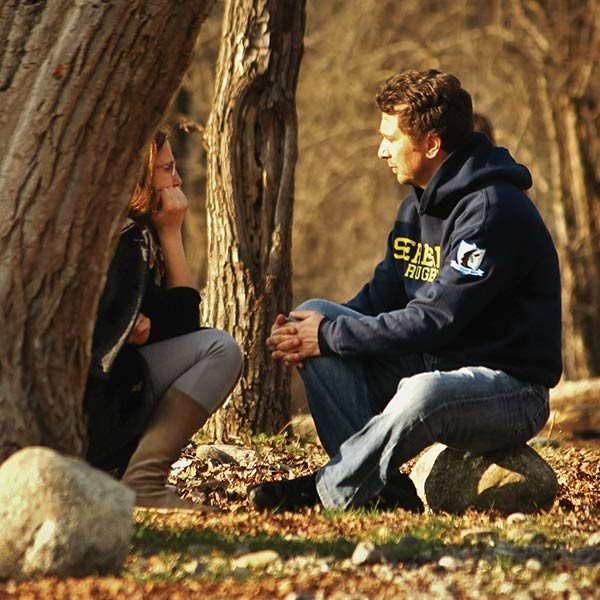 A man and a woman talk under a tree
