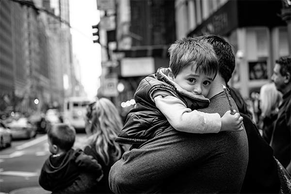 A man carrying a child on a New York City street.