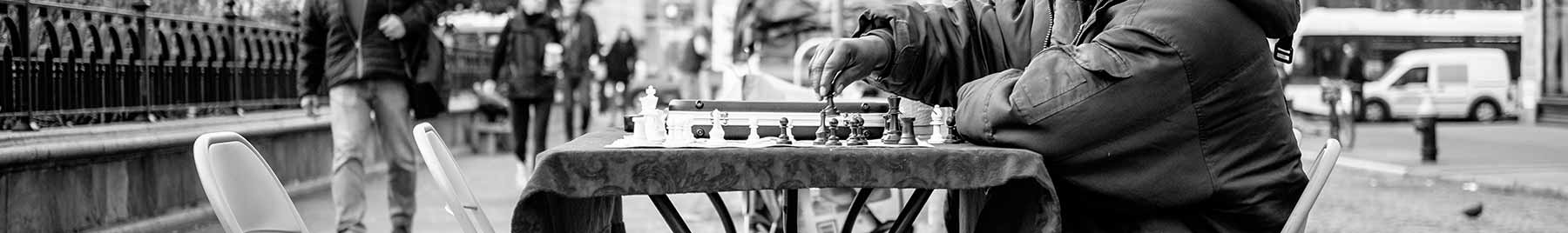An elderly man playing chess by himself on a New York City street.