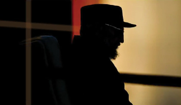 Fidel Castro's head and shoulders in silhouette against a mustard-colored wall.