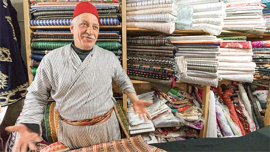 A middle-eastern shopkeeper with bolts of colorful cloth