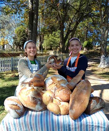 two women in front of several loaves of homemade bread