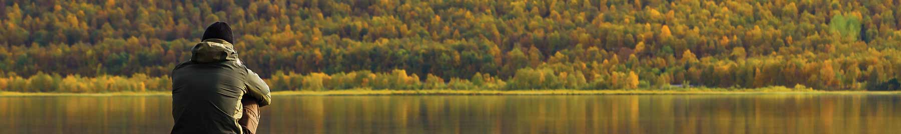 Man sitting on a rock looking at reflection of autumn trees in lake