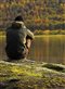 Man sitting on a rock looking at reflection of autumn trees in lake