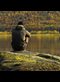 Man sitting on a rock looking at reflection of autumn trees in lake