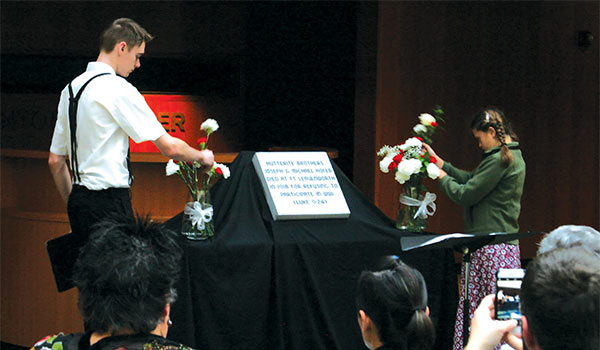 a Hutterite boy and a Bruderhof girl lay flowers in remembrance of men who refused to fight in WWI