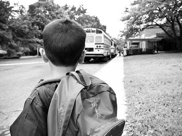 a black and white photograph of a boy looking at a school bus