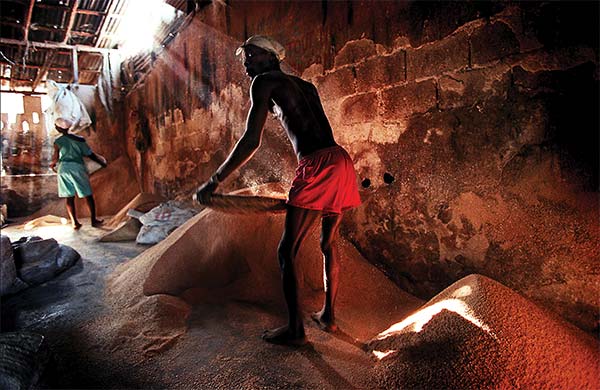 two people sifting grain in a dark room lit by sun rays: Carl Juste,  A Day’s Work, Port-au-Prince, Haiti