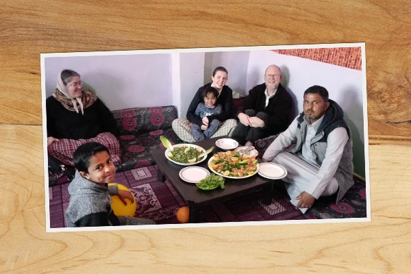 a photo on a wooden table of people gathered on the floor around a dish of Middle Eastern food