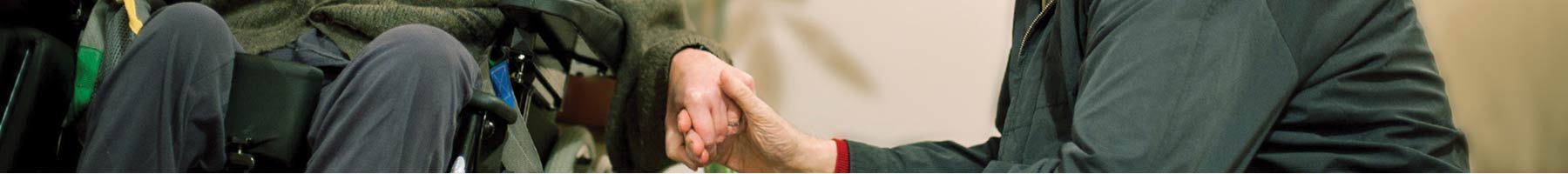 Man in a wheelchair holds the hand of a caregiver