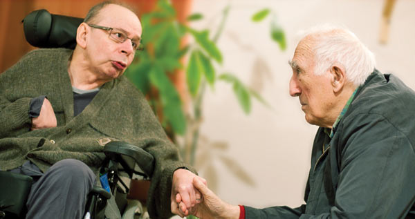 Jean Vanier holds the hand of an elderly man. 