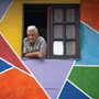 old man looking out of a window in a colorful wall