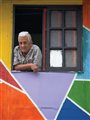 old man looking out of a window in a colorful wall