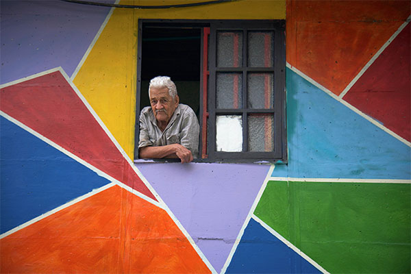 old man looking out of a window in a colorful wall
