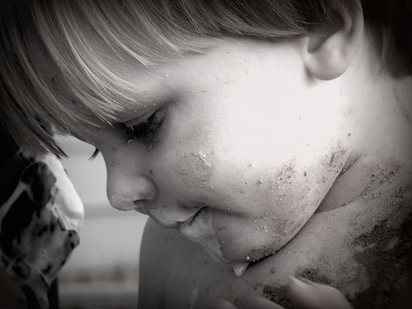 a black and white photograph of a boy with sand on his face