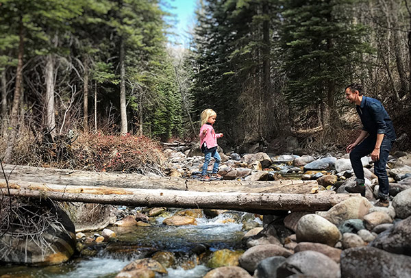 a girl walking across a log over a stream to her dad