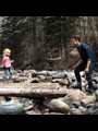 a girl walking across a log over a stream to her dad