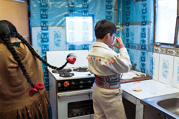 photograph of an Aymara boy drinking water in a small kitchen