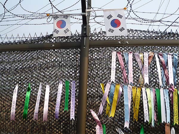 colorful ribbons with Korean writing on them tied on a barbed wire fence