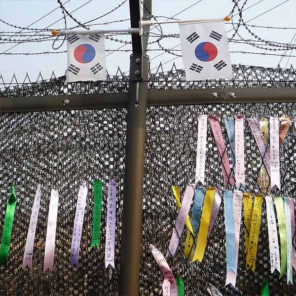colorful ribbons with Korean writing on them tied on a barbed wire fence