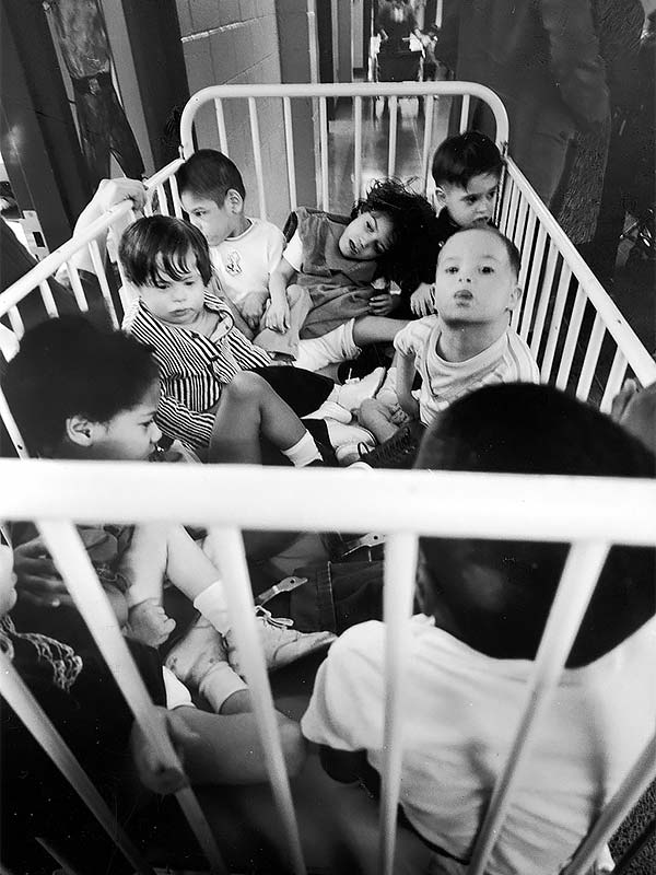 black and white photo of seight children crowded in a white metal crib