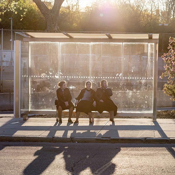 three girls sitting in a bus stop shelter in sunlight