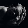 black and white photo of a mans hands holding a newborn baby