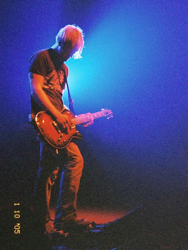 man playing a electric guitar backlit by spotlights