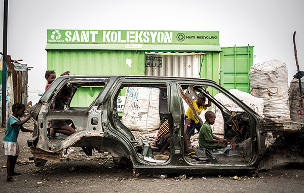 kids playing in the shell of a car in a Haitian scrapyard