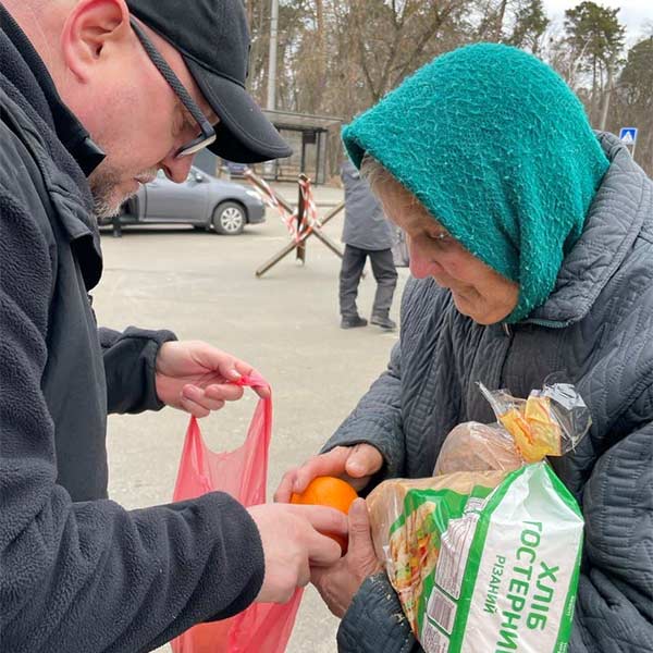 man giving bread and oranges to an older woman in a teal headscarf