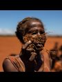 a woman holds part of a dead corn plant in a field covered with red sand