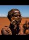 a woman holds part of a dead corn plant in a field covered with red sand