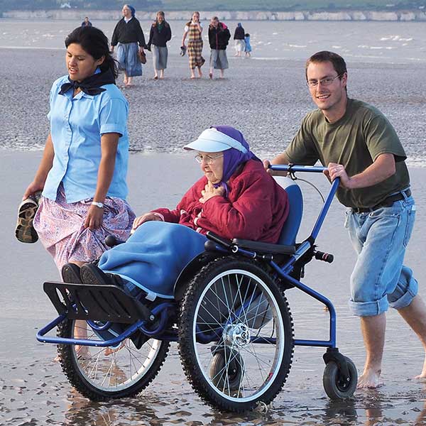 elderly person being pushed in a wheelchair by the beach