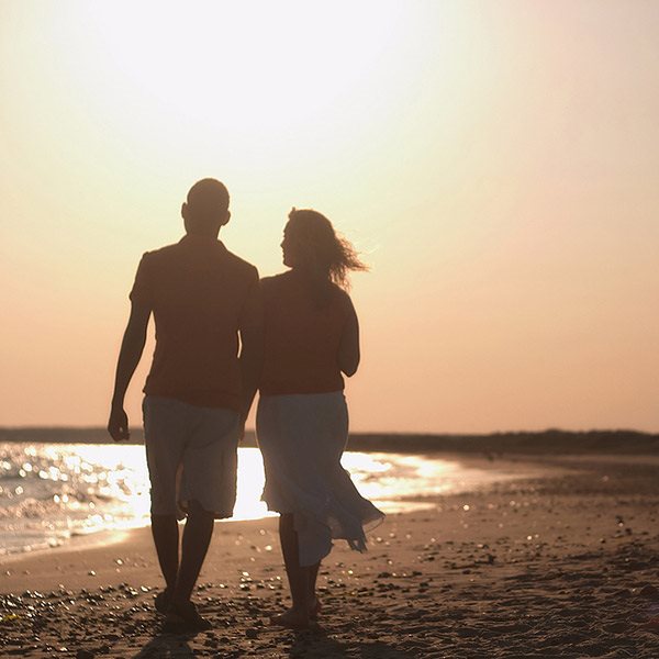 a couple strolls toward an orange sunset